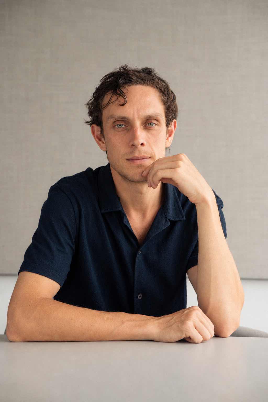 Liam Desroy sitting at a white table in a navy shirt, chin resting on his hand